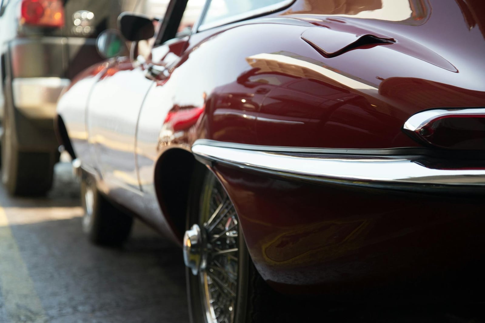 Close-up of the rear haunch, chrome bumper and wire wheel of a deep red Jaguar E-Type