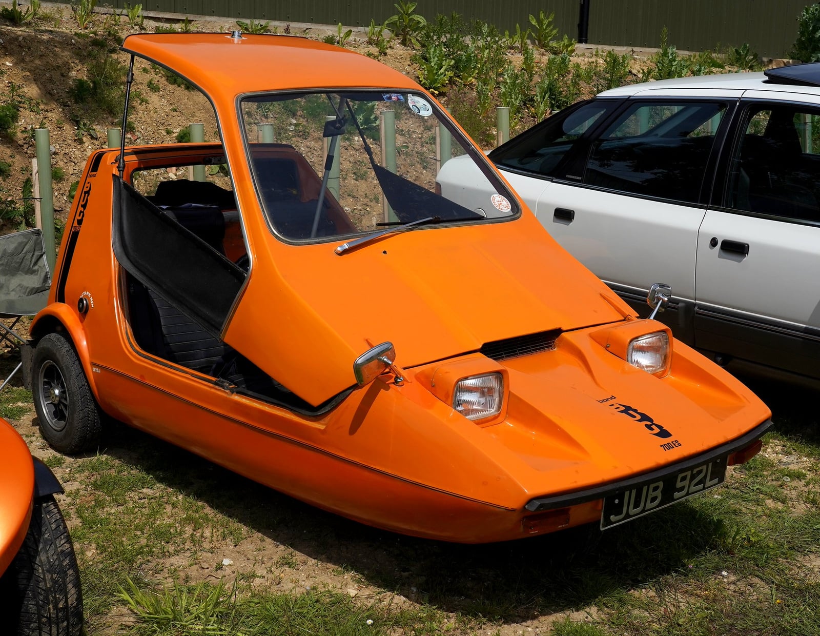An orange Bond Bug three-wheeler at a show, front three-quarter view showing the wedge profile and the open doorless side with the seats visible