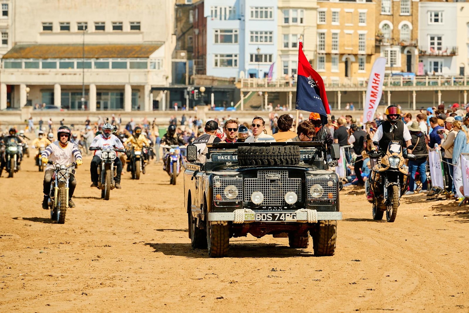 An early Land Rover Series I leading a parade along a beach