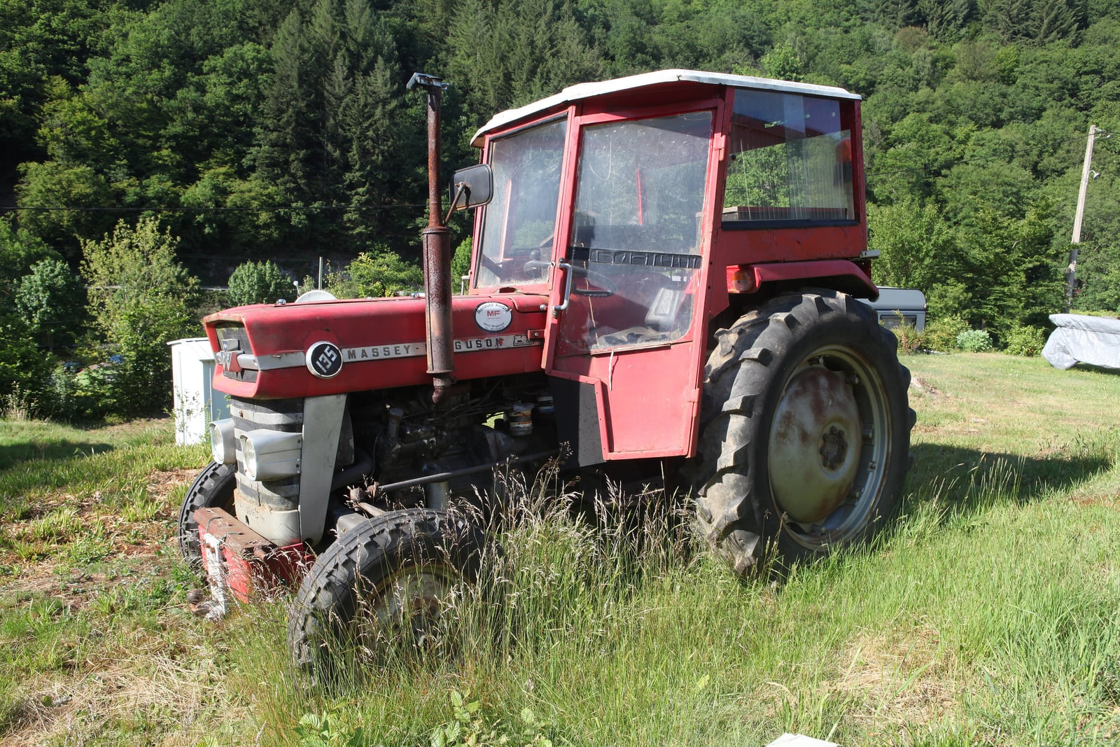 A red Massey Ferguson 135 fitted with a cab, three-quarter front view, standing in a grassy field