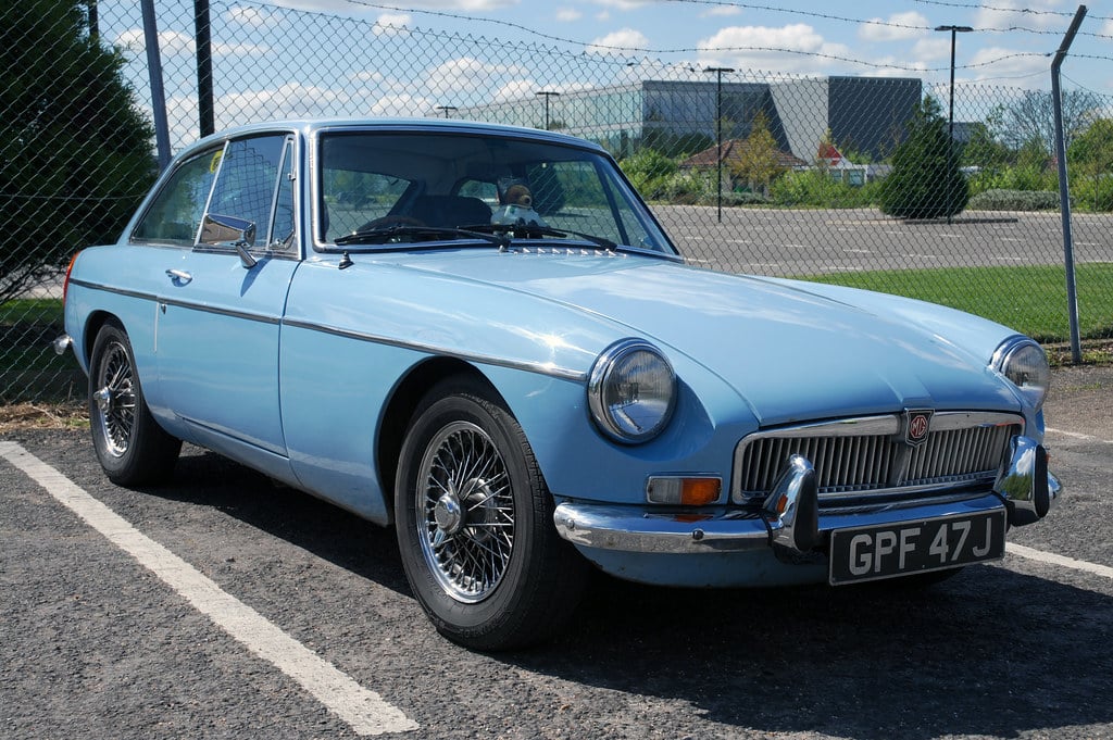 A light blue MG MGB GT with wire wheels, front three-quarter view