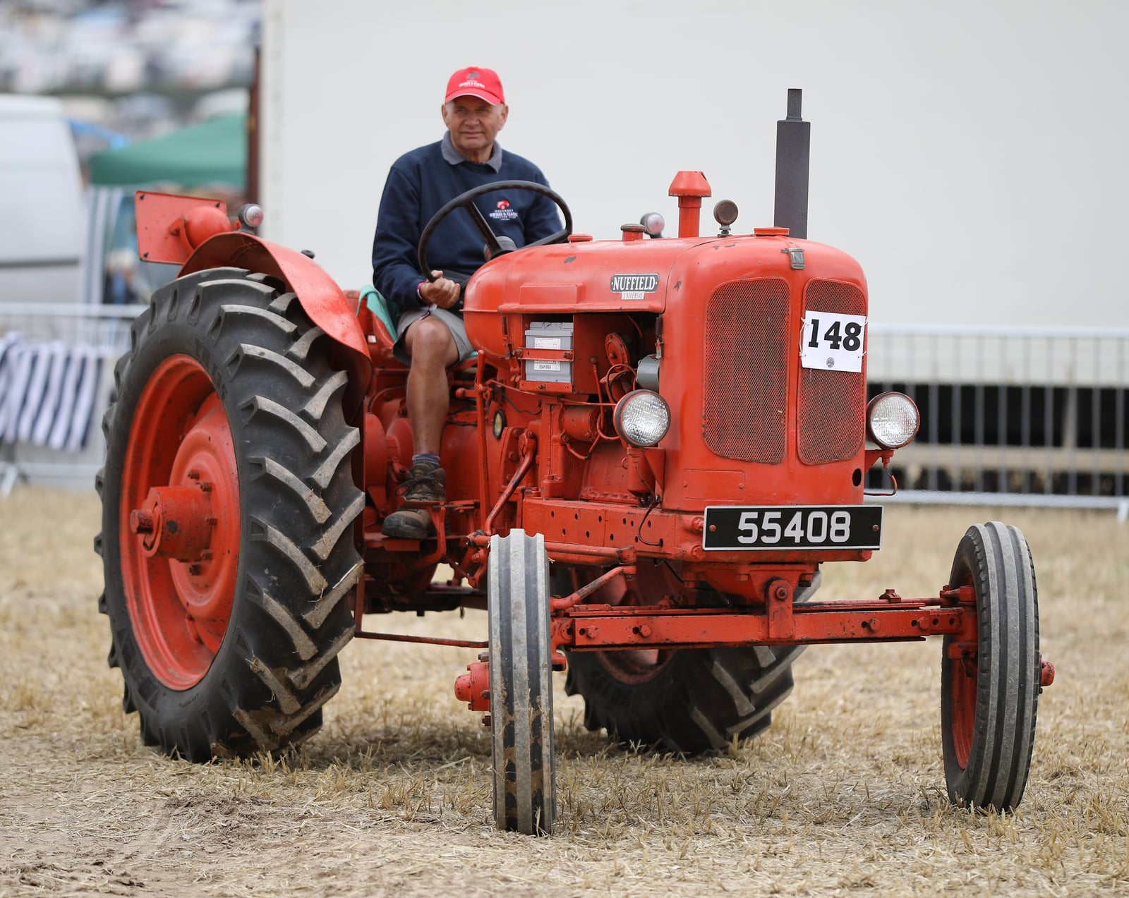 An orange Nuffield Universal being driven on a show field, a man at the wheel, registration 55408