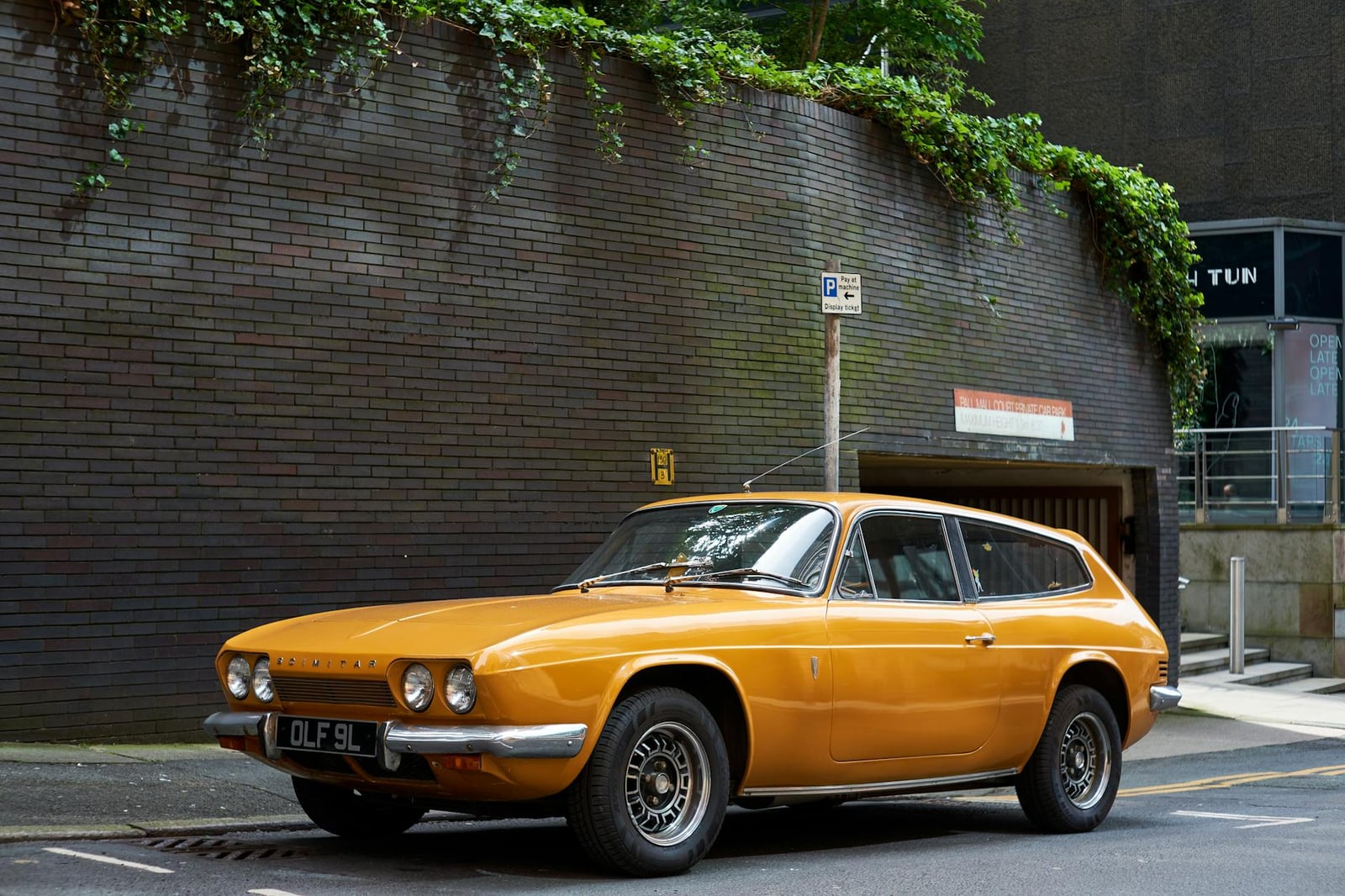 An orange Reliant Scimitar GTE sporting estate, front three-quarter view, parked beside a brick wall